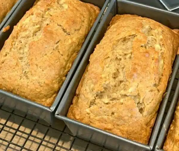Slice of moist apple bread on a wooden cutting board with apples in the background