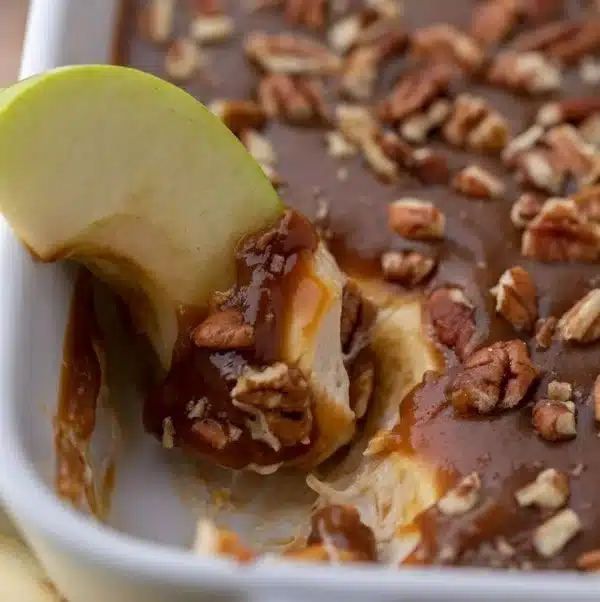 Creamy caramel apple cheesecake dip in a bowl with apple slices.