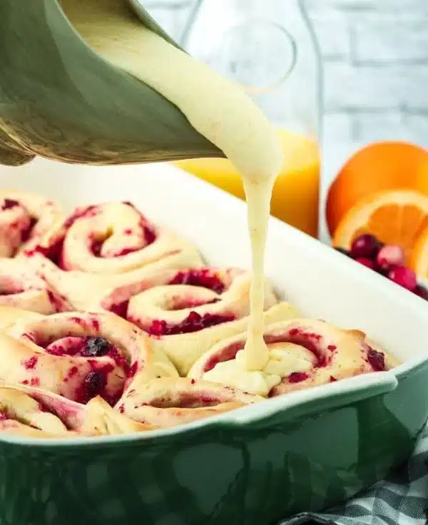 Freshly baked cranberry orange sweet rolls with glaze on a wooden table.
