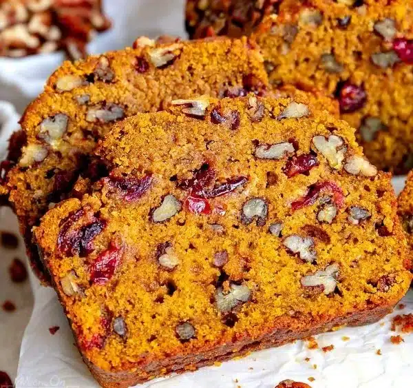 Slice of cranberry pecan pumpkin bread on a wooden cutting board