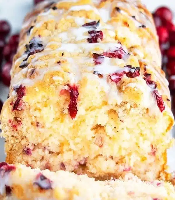 Slice of orange-glazed cranberry bread on a wooden cutting board