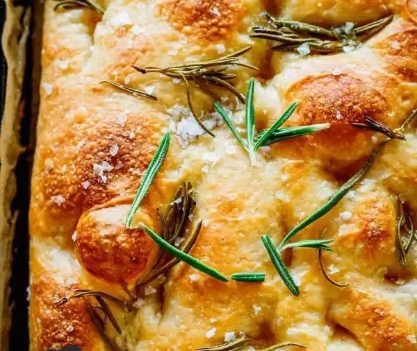 A freshly baked sourdough focaccia bread topped with herbs and olive oil.